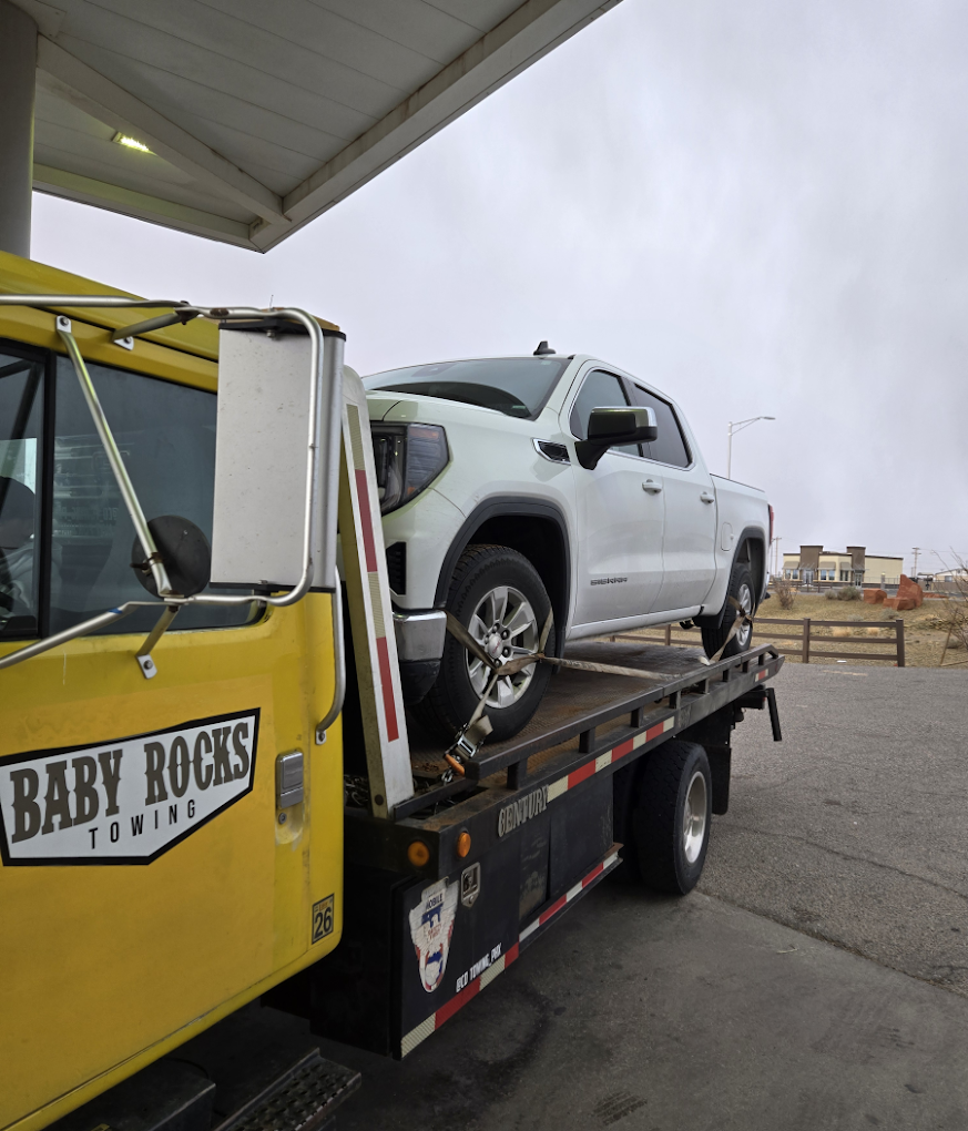 A yellow Baby Rocks Towing flatbed truck securely transporting a larger passenger vehicle, demonstrating reliable local towing and roadside recovery services.